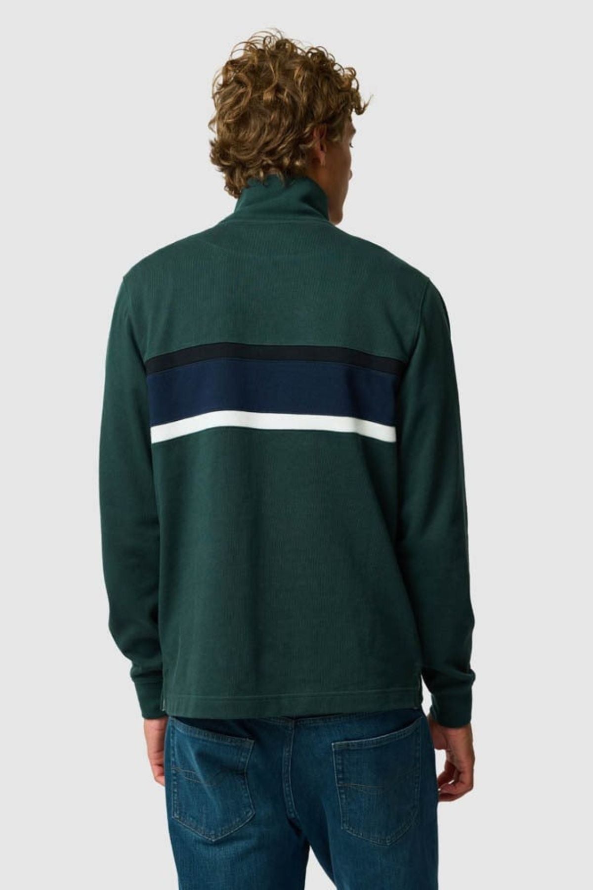 A person with curly hair is shown from the back, wearing the Rodd & Gunn Chesterfield Sweat—a dark green sustainable top with navy and white stripes across the upper back—paired with blue jeans against a plain light gray background.