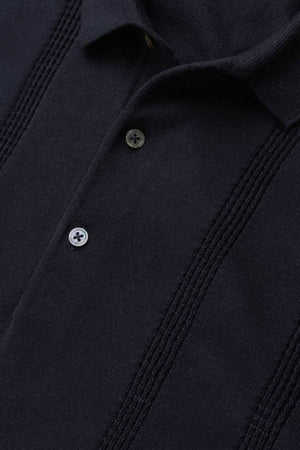 Close-up of the Rodd & Gunn Brooklands Knit, a dark navy Australian cotton polo with a collar, two buttons, and vertical textured stripes.