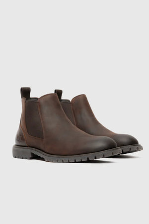 The Rodd & Gunn Clearmont Chelsea Boot, crafted in brown leather with black elastic side panels and black rubber soles for comfort, is displayed on a light gray background.