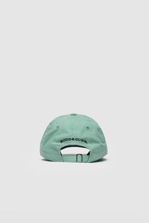 The Rodd & Gunn Gunn Cap is a light green cotton twill cap shown from the back, with the "RODD & GUNN" logo embroidered in black above an adjustable strap. Set against a plain light gray background, it delivers a casual yet polished style.