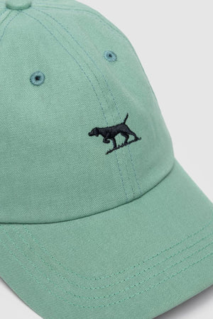 The Rodd & Gunn Gunn Cap is a light green cotton twill hat featuring visible stitching and a small black embroidered dog logo on the front, offering classic style and quality craftsmanship.