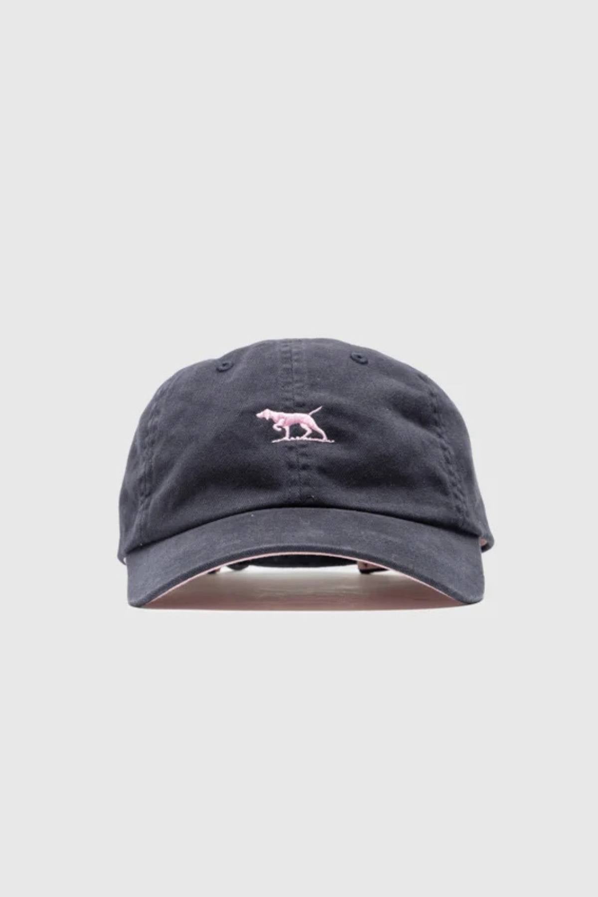 The Rodd & Gunn Gunn Cap Petite is a black cotton twill cap with a small pink dinosaur embroidered on the front and an adjustable back strap, shown against a plain light gray background.