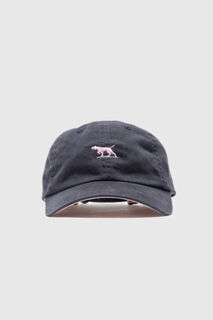 The Rodd & Gunn Gunn Cap Petite is a black cotton twill cap with a small pink dinosaur embroidered on the front and an adjustable back strap, shown against a plain light gray background.