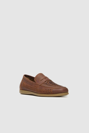 The Rodd & Gunn Gisbourne Huarache Slip On, a brown leather loafer with woven side and top detailing, low heel, and light beige sole, is shown on a plain light gray background—perfect breathable summer footwear.