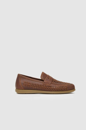 The Rodd & Gunn Gisbourne Huarache Slip On features brown leather with woven side and top detailing, a flat sole, and a penny slot on the upper—shown against a light gray background. Ideal breathable summer shoes.