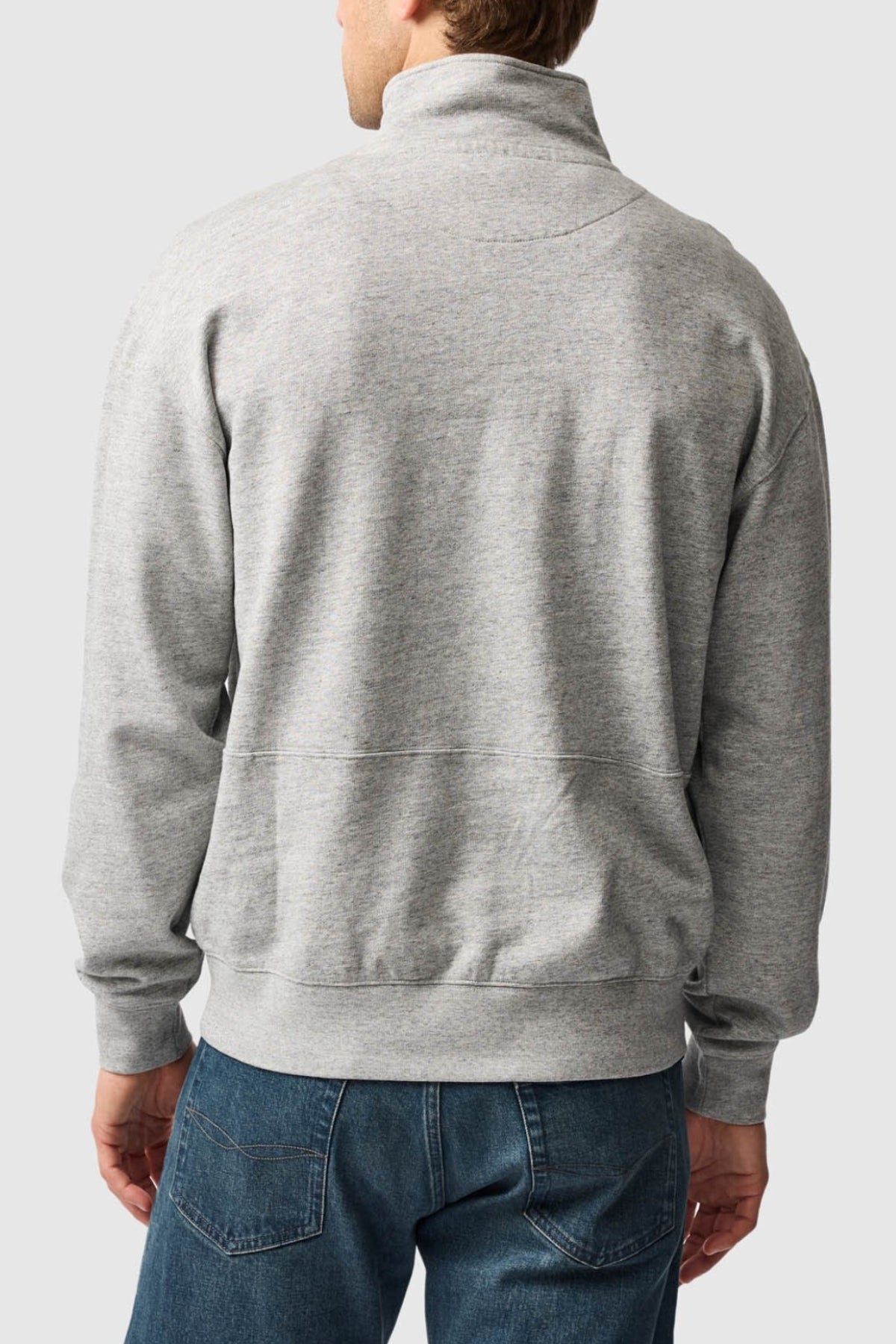 A person is shown from the back wearing a light gray Rodd & Gunn Milford Sound Sweat featuring a premium YKK metal zip, paired with blue jeans, standing against a plain light background.