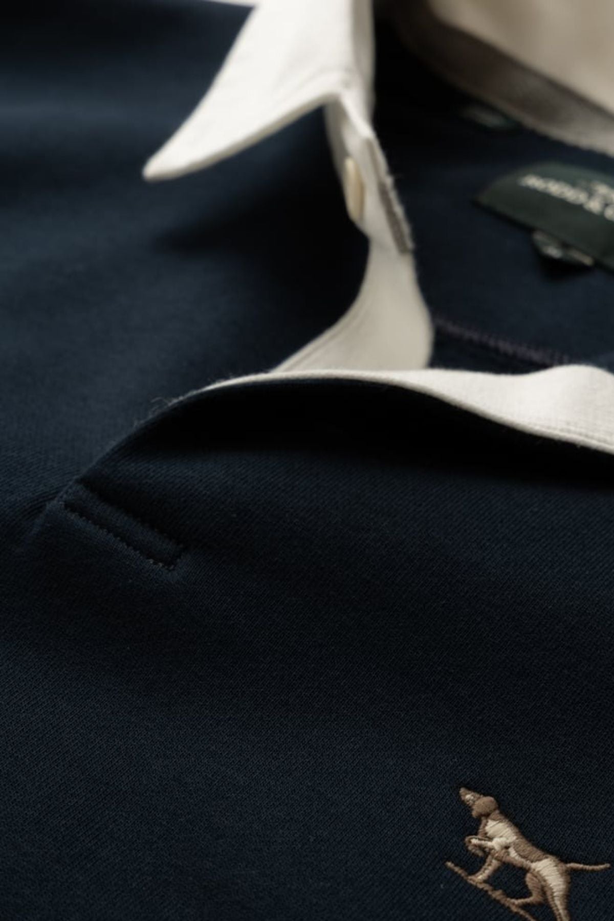 Close-up of a navy blue Rodd & Gunn polo shirt with a white collar and small chest logo, partially unbuttoned to reveal the label—ideal for layering under the Rodd & Gunn Otago Sweat.