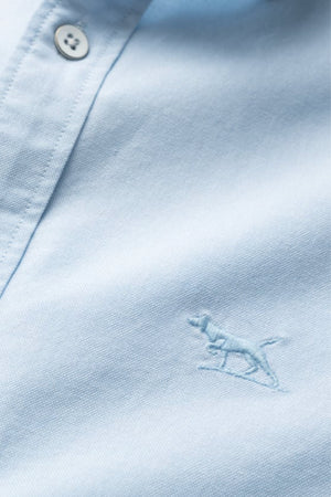 Close-up of the Rodd & Gunn Gunn Oxford Sports Fit Shirt in light blue cotton, featuring white buttons and an embroidered dog outline near the hem.