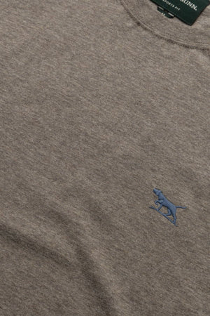 A close-up of the heather gray Rodd & Gunn The Gunn Tee 2.0, featuring a small blue embroidered dog logo on the chest, breathable jersey fabric texture, and a glimpse of the green neck tag.