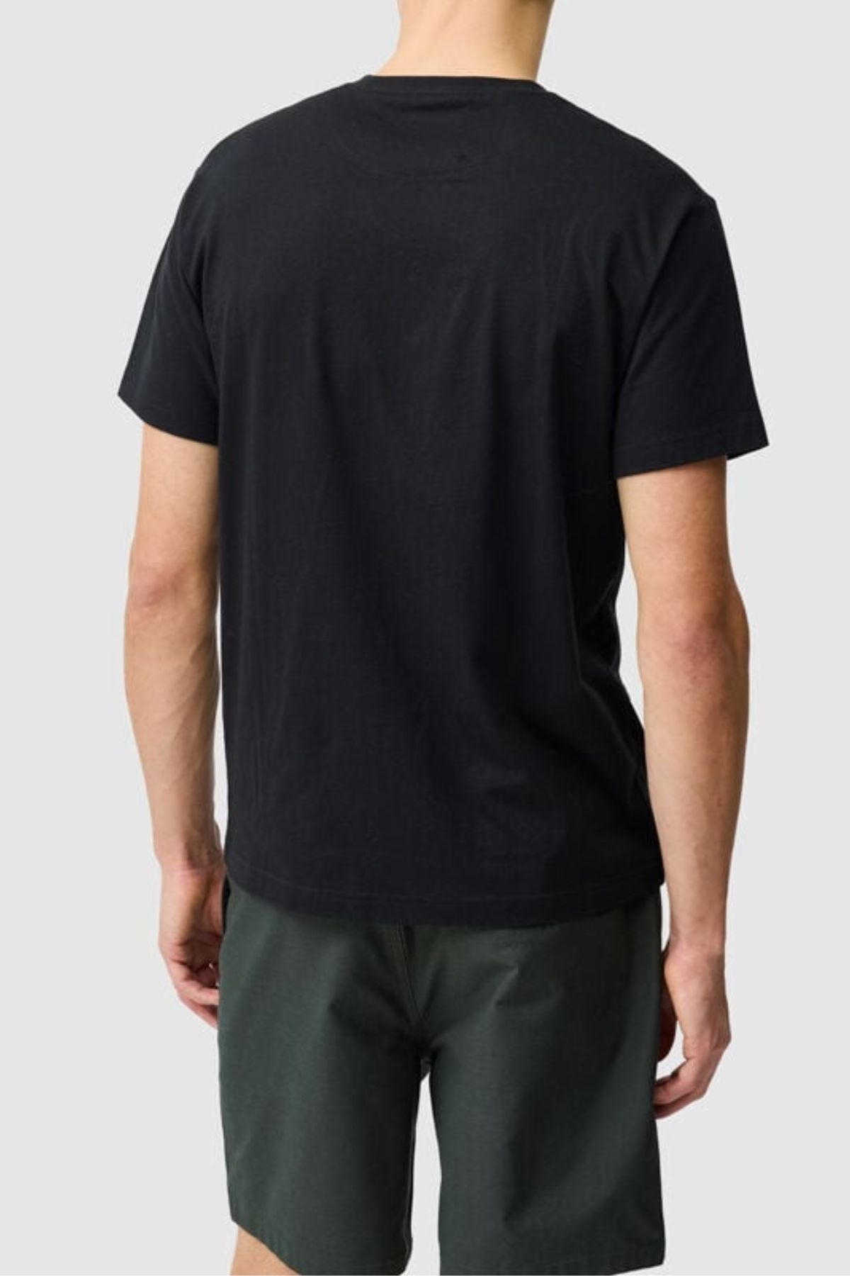 A person stands with their back to the camera, wearing a black Rodd & Gunn The Logo Tee 2.0 and dark green shorts, set against a light grey background.
