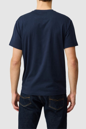 A person is shown from the back against a light gray background, wearing the Rodd & Gunn The Logo Tee 2.0 in plain navy blue 100% cotton sports fit and dark blue jeans.