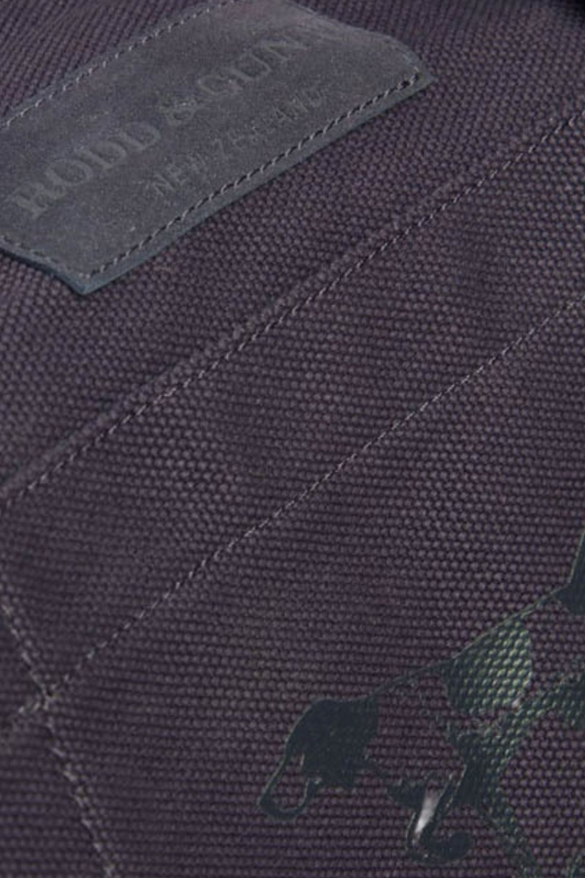 Close-up of the Rodd & Gunn Ponsonby Road Duffle Bag in dark cotton canvas, featuring visible stitching, a leather patch with a partial logo, and a subtle running dog graphic in the lower right corner.
