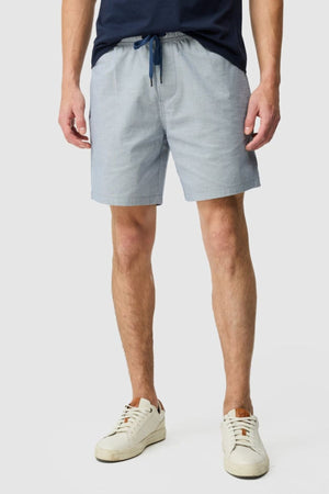 A person wearing Rodd & Gunn Resort Short in light blue cotton with an elastic waist stands against a plain light gray background. Only the lower torso and legs are visible.