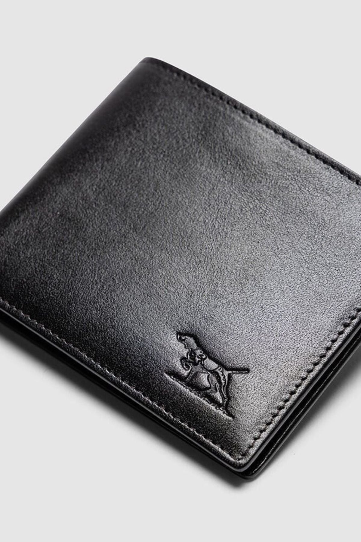 The Rodd & Gunn Wakefield Bi-Fold Wallet is a sleek black Italian leather wallet with stitched edges and an embossed dog outline on the lower right corner, shown against a light gray background.