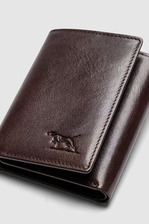 The Rodd & Gunn Westport Tri Fold Wallet is crafted from dark brown Italian leather with a smooth finish and features an embossed dog logo on the lower front, shown against a light gray background.