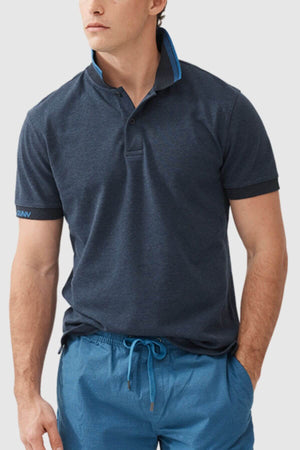 A man wears the Rodd & Gunn Masterton Sports Fit Polo in navy USA cotton, collar partially popped with light blue trim, paired with slim fit drawstring shorts, standing against a plain light background.