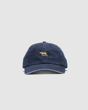 The Rodd & Gunn Gunn Cap in blue denim is made from heavy-duty cotton twill and features a small yellow embroidered animal on the front, set against a plain light gray background.