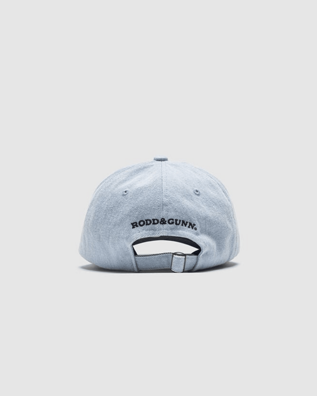 A Rodd & Gunn Gunn Cap in light blue, crafted from heavy-duty cotton twill, is seen from the back with "RODD & GUNN." embroidered above the adjustable strap against a plain light gray background.