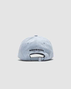 A Rodd & Gunn Gunn Cap in light blue, crafted from heavy-duty cotton twill, is seen from the back with "RODD & GUNN." embroidered above the adjustable strap against a plain light gray background.