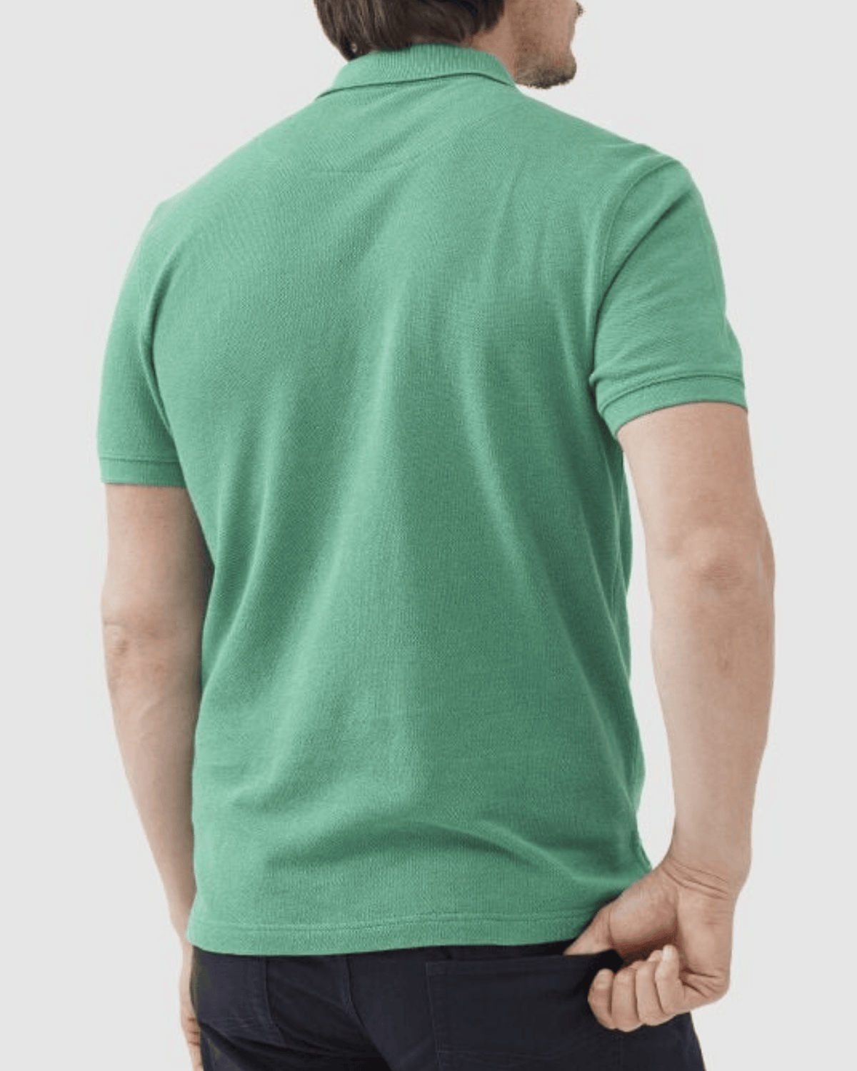 A person with short hair, seen from the back wearing dark pants and a modern fit, short-sleeved green Rodd & Gunn The Gunn Polo made from Australian Cotton, is turned away while holding the shirt's bottom with one hand.