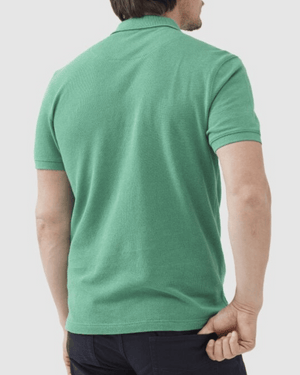 A person with short hair, seen from the back wearing dark pants and a modern fit, short-sleeved green Rodd & Gunn The Gunn Polo made from Australian Cotton, is turned away while holding the shirt's bottom with one hand.