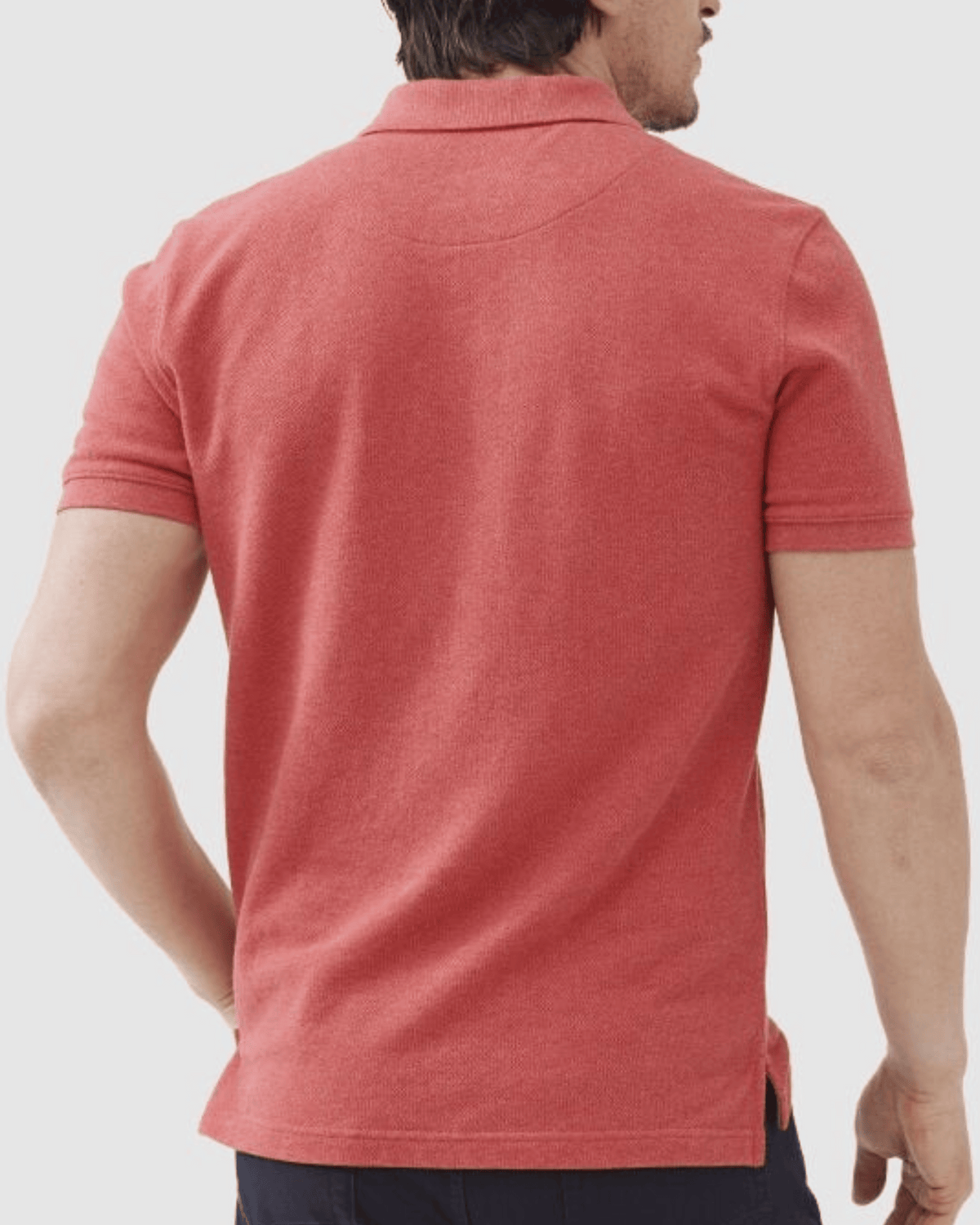 A man is seen from behind wearing the Rodd & Gunn The Gunn Polo in red, a modern fit, short-sleeved shirt made of Australian cotton, paired with dark pants and his right hand resting on his hip.
