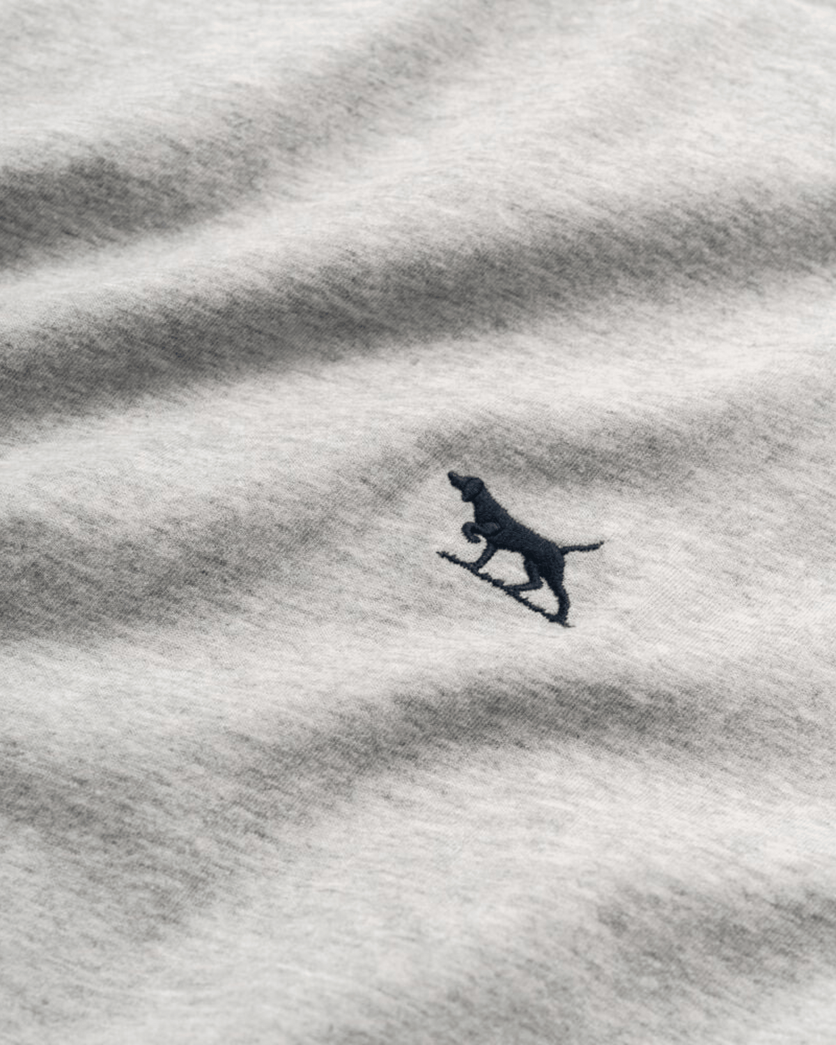 Close-up of light grey Australian Cotton Rodd & Gunn The Gunn T-Shirt, featuring a small, dark embroidered dog silhouette on textured material with visible ruffles.