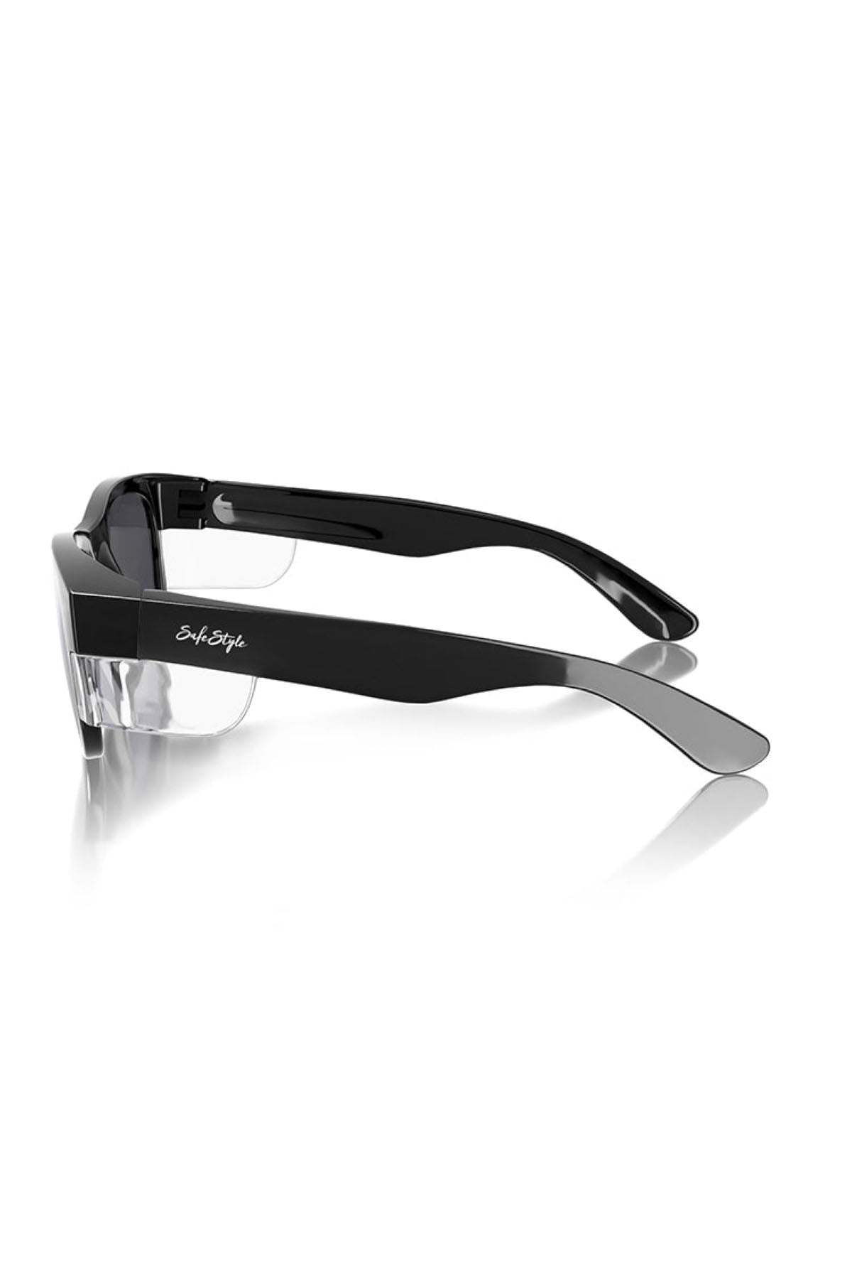Side view of SafeStyle Classics Black Frame Polarised Lens sunglasses with clear UV-protection lenses, featuring thick temples and a reflective silver logo on one arm. The sleek black glasses rest atop a white reflective surface.