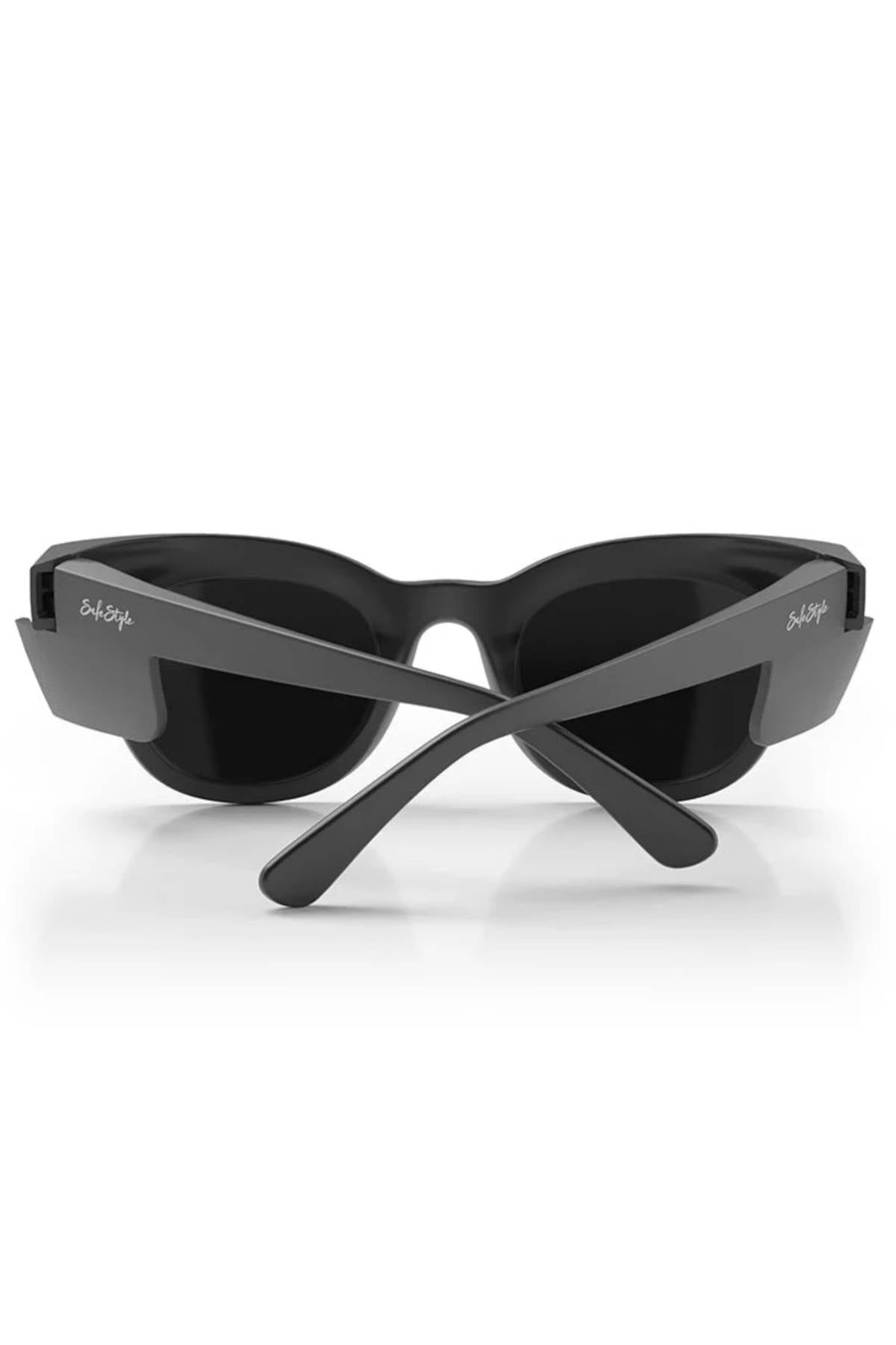 A pair of SafeStyle Harps Matte Black Frame Polarised Lens sunglasses viewed from the back, arms crossed. The brand name appears in white on the temples. The background is plain white.