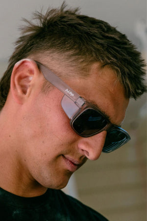 A man with short brown hair wears Safestyle Fusions XL Matte Graphite Frame Polarised Lens sunglasses and a black shirt, looking slightly downward with a neutral expression.