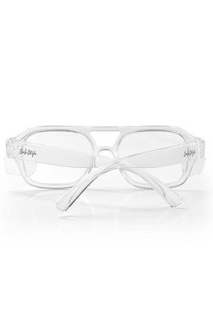 The Safestyle Skylines Clear Frame Clear Lens features clear rectangular eyeglasses with transparent frames and arms, crafted from shatterproof polycarbonate. Displayed arms crossed on a white surface, "InkStyle" is scripted in black on the left temple.