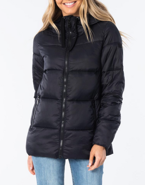 A person wearing a Rip Curl Anti Series Insulated Jacket in black, complete with a hood, stands against a plain white background, smiling. The insulated jacket showcases a front zipper and zippered pockets. The individual is also sporting blue jeans, with light blonde hair partially covering their shoulders.