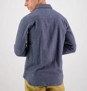 Wearing the Swanndri Ranch Rd Shirt, a 100% cotton, long-sleeved, button-up in blue, a person faces away from the camera. The perfectly tailored shirt pairs effortlessly with beige pants against a plain white background.