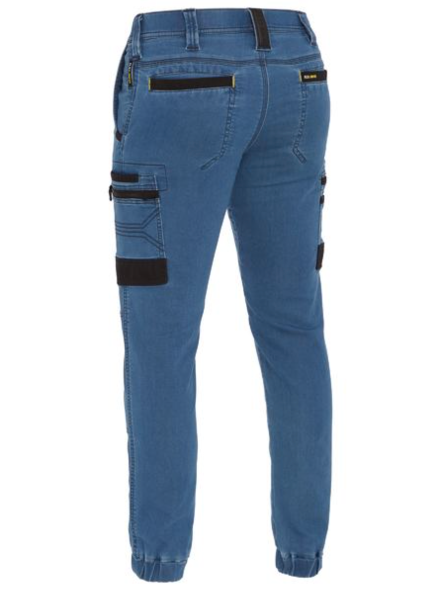 Seen from the back, the Bisley Flex & Move Stretch Denim Cargo Cuffed Pant in blue features black accents on pocket fasteners. With reinforced belt loops, multiple pockets—including large side pockets—and elastic ankle cuffs for a modern fit.
