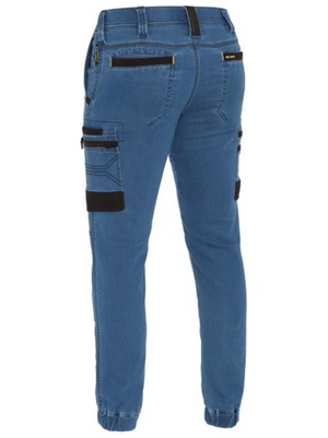 Seen from the back, the Bisley Flex & Move Stretch Denim Cargo Cuffed Pant in blue features black accents on pocket fasteners. With reinforced belt loops, multiple pockets—including large side pockets—and elastic ankle cuffs for a modern fit.