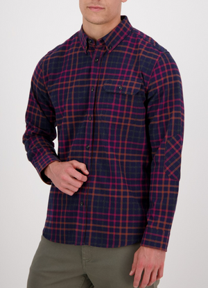 A man wears the Swanndri Eastcott Shirt—classic fit, long-sleeve, navy, red, and orange plaid in 100% cotton—paired with olive green pants, standing against a plain white background.