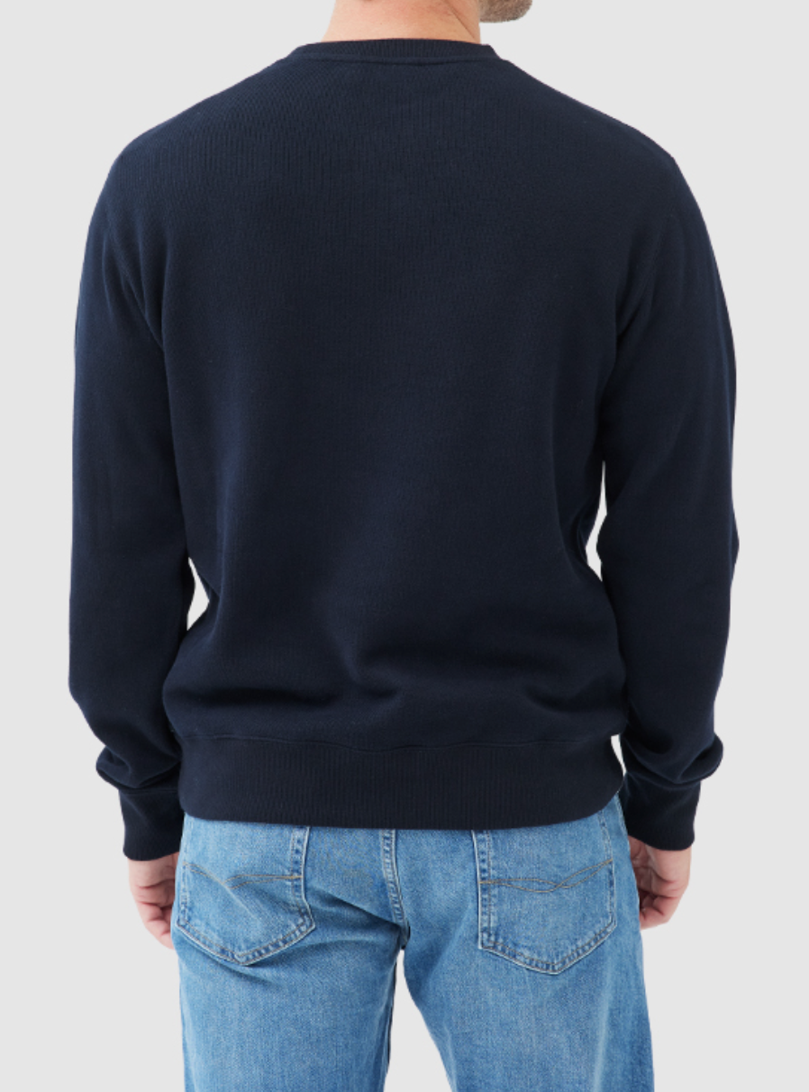 A person is seen from the back wearing the Rodd & Gunn Gunn Crew Neck Sweat in dark navy blue with light blue jeans against a plain light gray background.