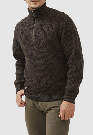 A man wears the Rodd & Gunn Challis Knit, a dark brown lambswool half-zip sweater, paired with olive green pants and poses with one hand near his waist.