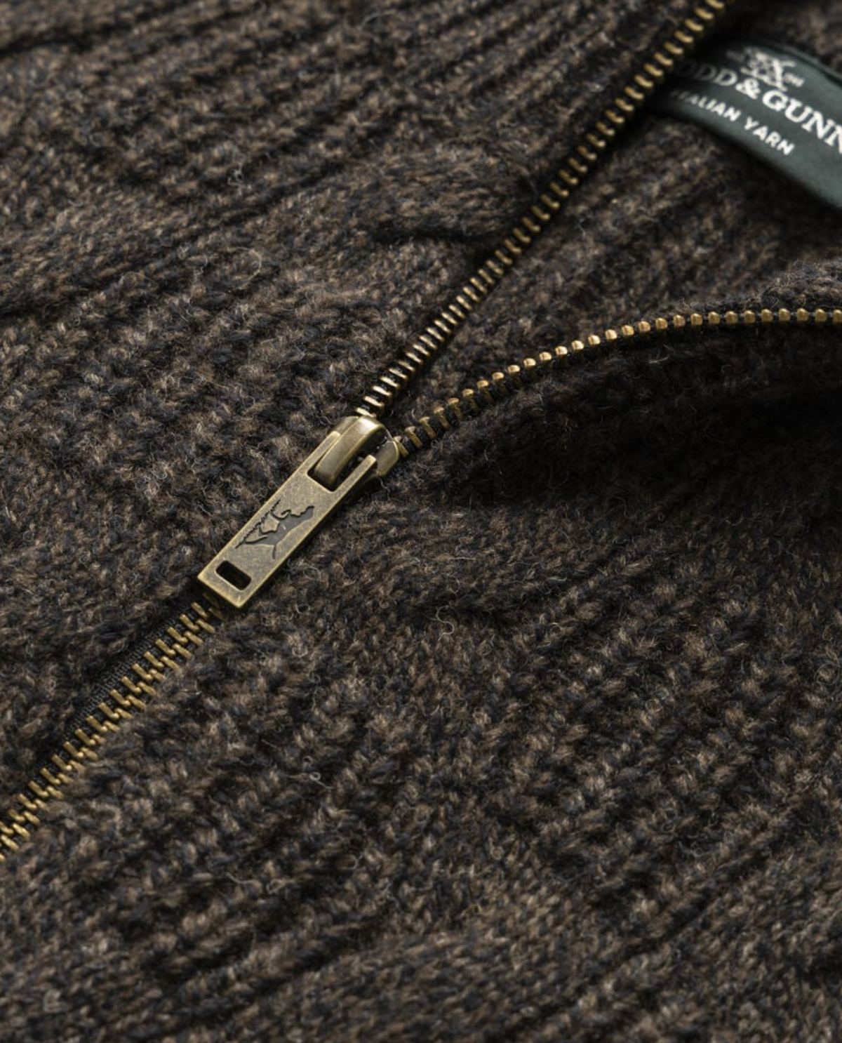 Close-up of the Rodd & Gunn Challis Knit sweater in textured brown lambswool, featuring a partially open brass zipper and a visible section of the fabric tag near the collar.