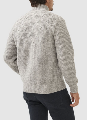 A person is wearing the Rodd & Gunn Challis Knit, a light gray textured cable knit sweater with a geometric pattern on the upper back. It's stylishly paired with dark blue jeans, set against a plain white background.