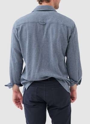 A person in a blue checked Rodd & Gunn Pentland Hills Shirt, made of 100% cotton, and dark pants stands with their back to the camera. Their right hand is relaxed by their side.