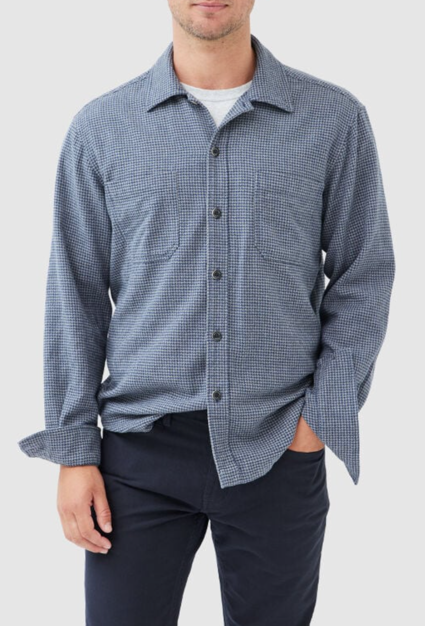 A person in a Rodd & Gunn Pentland Hills blue and black checkered long-sleeve shirt, made of 100% cotton, stands against a white background. The shirt has front buttons and two chest pockets, while their hand rests in their dark pants pocket.