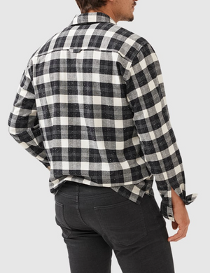 A man faces away, wearing the Rodd & Gunn Halfmoon Ave Shirtβcomfortable 100% cotton in black and white checksβand black jeans, standing against a light grey background.
