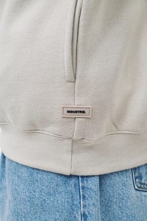 Close-up of a person wearing the Industrie The Del Sur Track Top in light beige with an oversized fit and a small label at the hem, paired with light blue denim jeans.