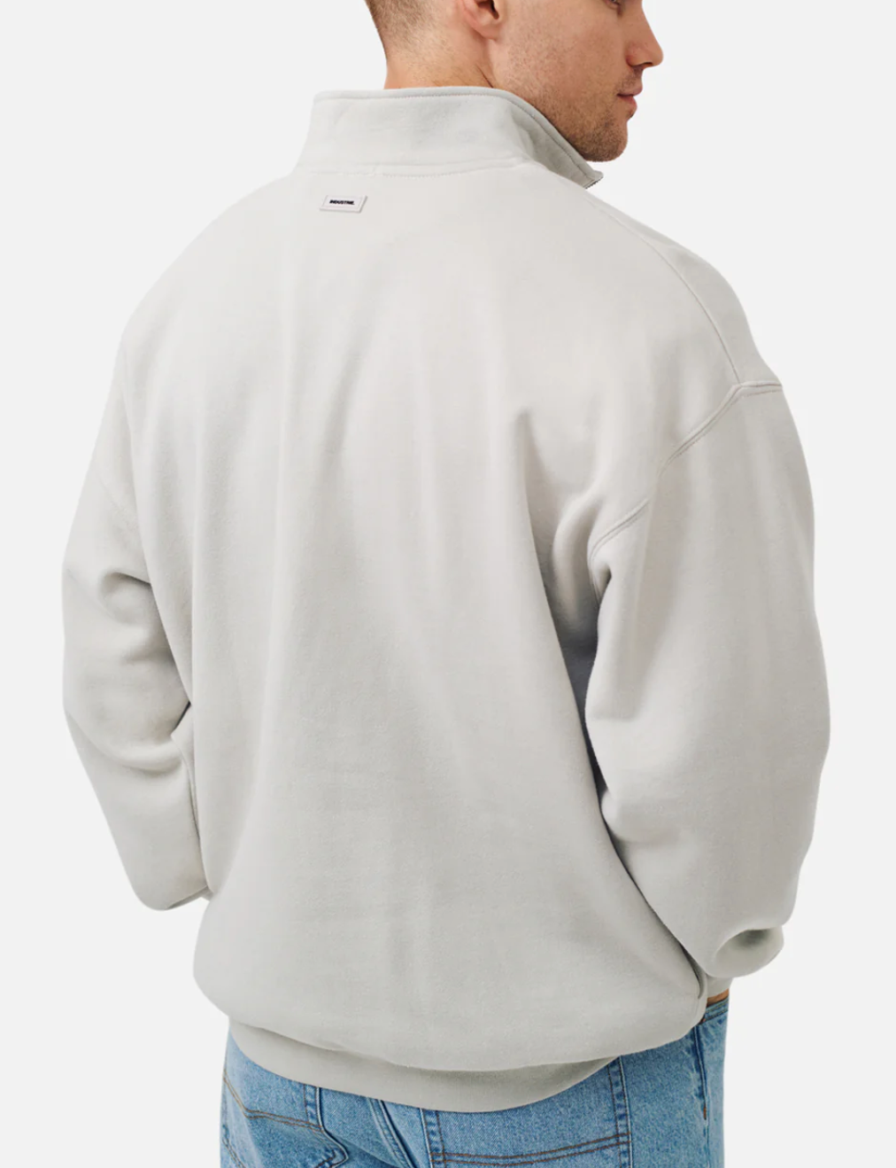 A man is shown from the back, hands in pockets, wearing the Industrie The Del Sur Track Top in light grey with a high collar and soft fleece lining, paired with blue jeans against a plain white background.
