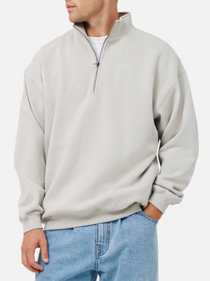 A person wears the Industrie The Del Sur Track Top, a light gray quarter-zip pullover with soft fleece lining, over a white T-shirt and light blue jeans, standing with one hand in their pocket against a plain background.