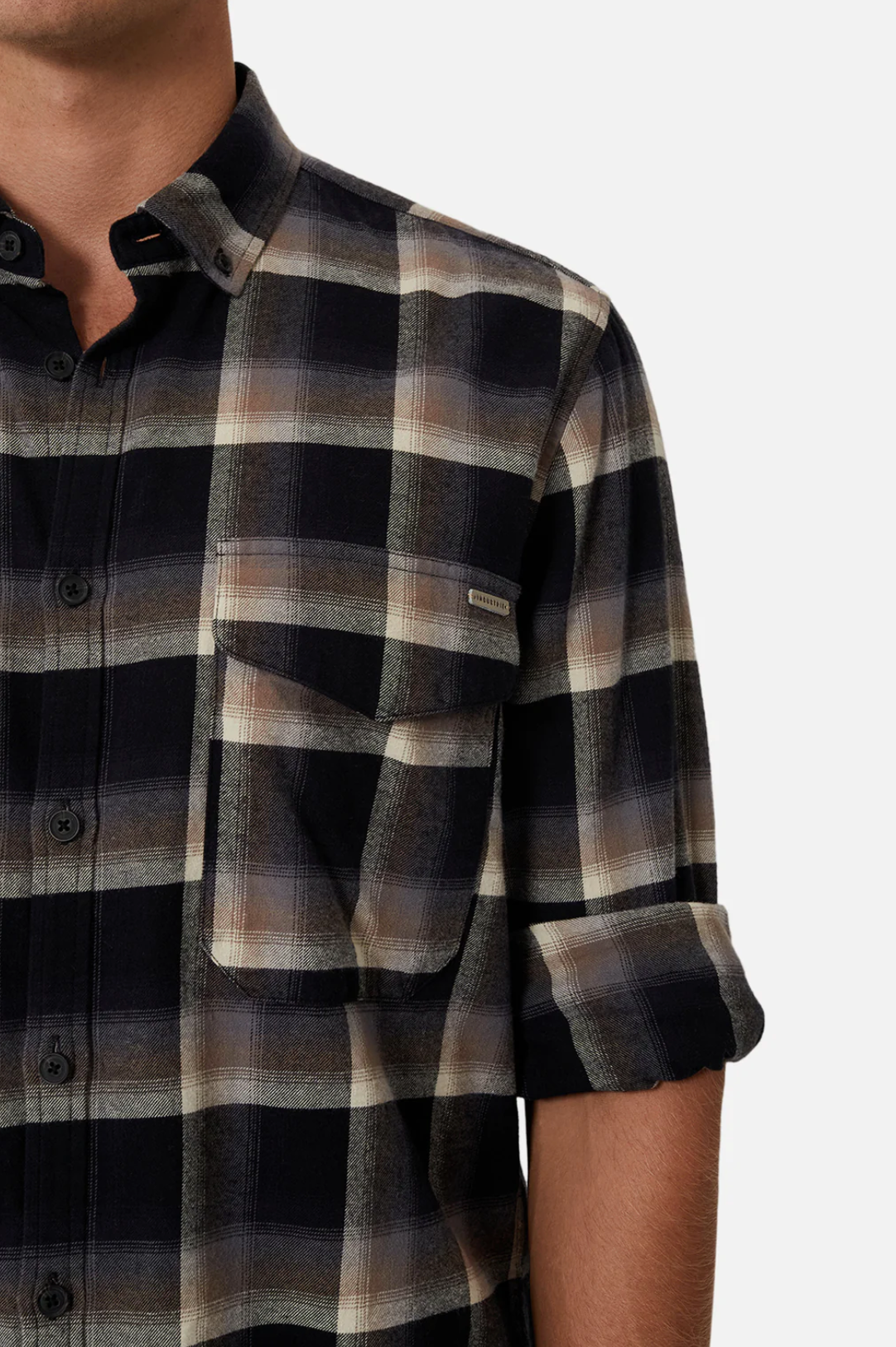 Close-up of a person wearing Industrie The Clifton Shirt, a regular-fit black, gray, and beige plaid button-up with rolled sleeves. Made from 100% cotton, it includes a chest pocket with a small tag. The person's face is not visible against the white background.