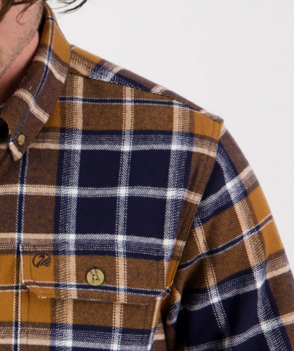 Close-up of the Swanndri Pencarrow Shacket—classic fit, plaid flannel in brown, navy blue, and white—with a buttoned chest pocket and part of a person's neck and shoulder visible.