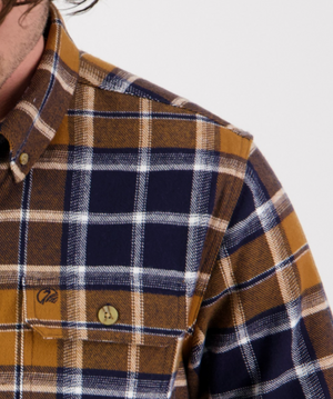 Close-up of the Swanndri Pencarrow Shacket—classic fit, plaid flannel in brown, navy blue, and white—with a buttoned chest pocket and part of a person's neck and shoulder visible.