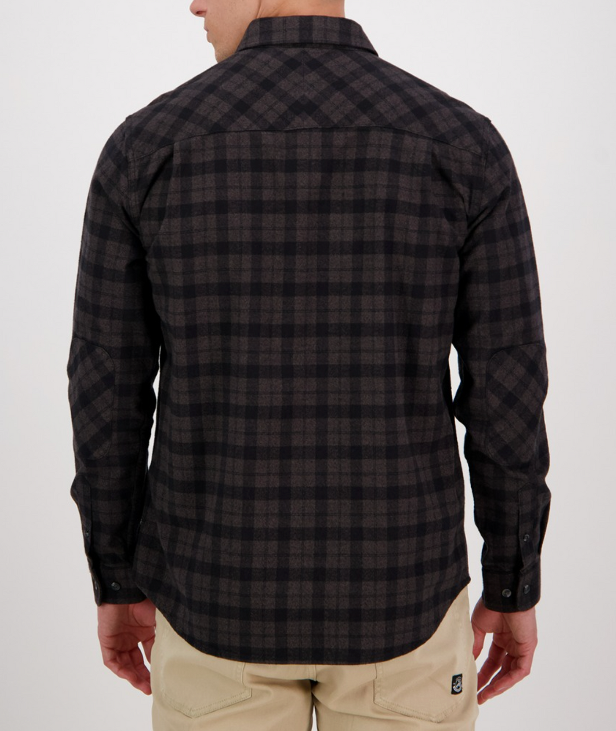 Wearing a Swanndri Port Road Shirt in dark plaid with long sleeves and beige pants, a person stands with their back to the camera against a plain, light background.